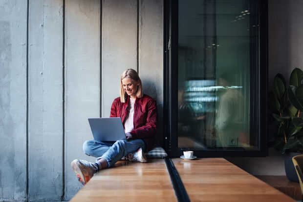 Frau sitzt mit Laptop in einem modernen Coworking Space und arbeitet an einem flexiblen Arbeitsplatz.